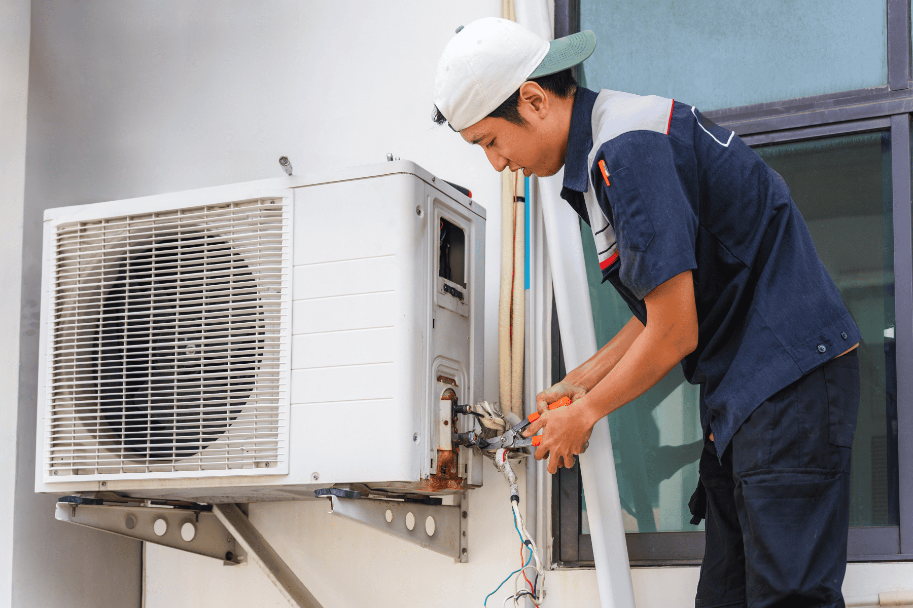 A technician in uniform repairs or installs a window AC unit beside a building window using tools, ensuring reliable cooling as part of various AC options available for homeowners.