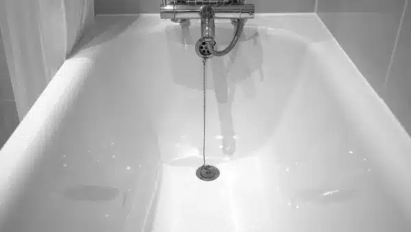 Close-up view of a clean, empty bathtub with a plug on a chain attached to the drain, under a mounted faucet—perfect for highlighting our professional Drain Clearing Service in Fairfax VA.