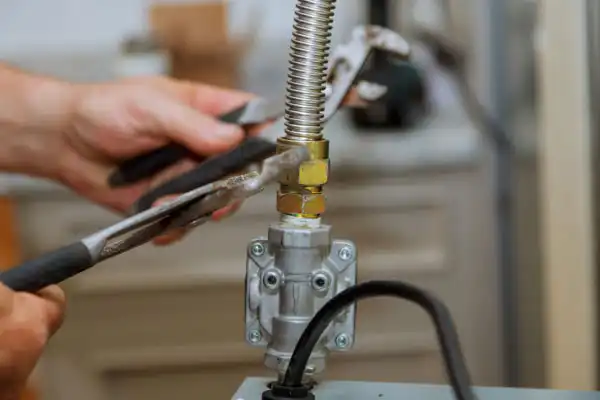 Hands using pliers to tighten a brass connector on a flexible gas line during a gas line installation in Fairfax VA, with tools and appliances visible in the background.