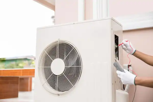 A person wearing white gloves uses a tool to check or repair the wiring of an outdoor air conditioning unit during heat pump maintenance in Fairfax VA.