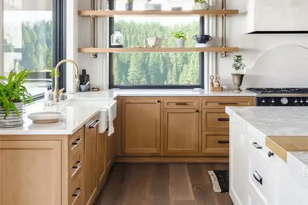 Modern kitchen with light wood cabinets, white countertops, open shelves holding plants and dishes, a large window with a forest view, and natural light filling the space—perfect for any Fairfax, VA home needing plumbing repair updates.