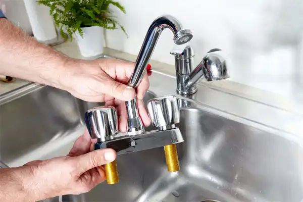 A person holds a new kitchen faucet above a stainless steel sink, preparing for a Kitchen Plumbing Installation in Fairfax VA.