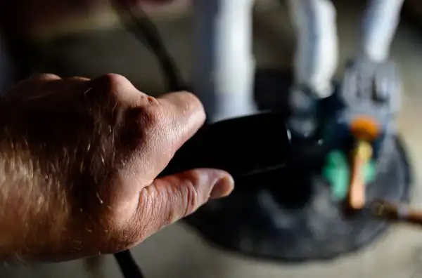 A close-up of a person's hand holding a black tool during a sump pump installation, with blurred mechanical parts and hoses in the background—captured on-site in Fairfax VA.