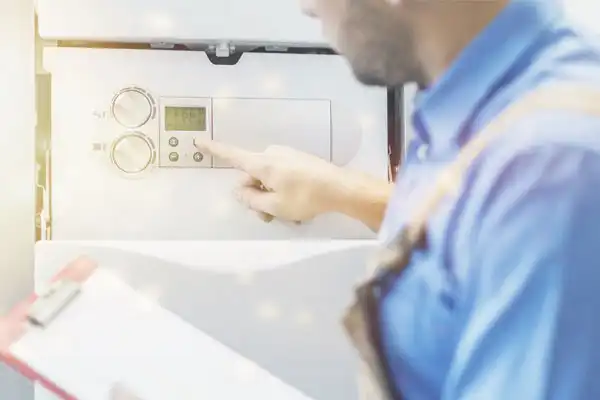 A person in work attire adjusts the settings on a tankless water heater installation control panel in Fairfax, VA, holding a clipboard in the other hand, with the focus on their actions.