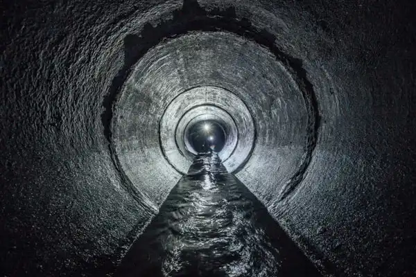 A circular underground tunnel in Fairfax VA with water flowing through the center, illuminated by light at the far end—a glimpse into modern trenchless sewer line installation.