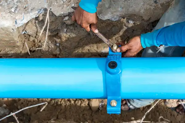A person in a blue shirt tightens bolts on a blue underground water pipe using a wrench, performing Water Line Repair in Fairfax VA.