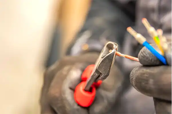 A person wearing gloves uses wire cutters to strip insulation from electrical wires during an electrical installation in Fairfax VA.