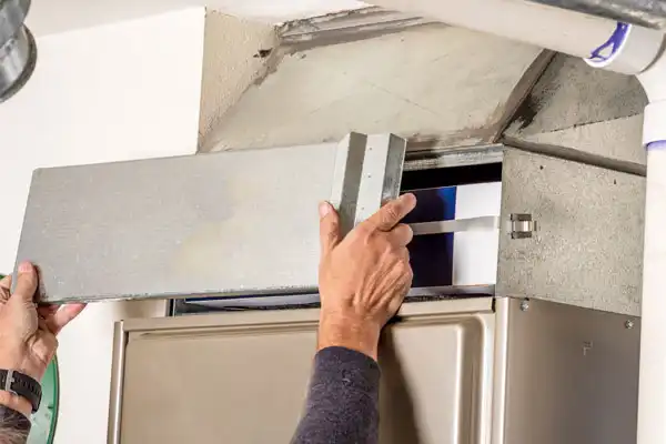 A person in Fairfax, VA, removes a metal panel from a furnace to access the air filter inside during furnace maintenance.