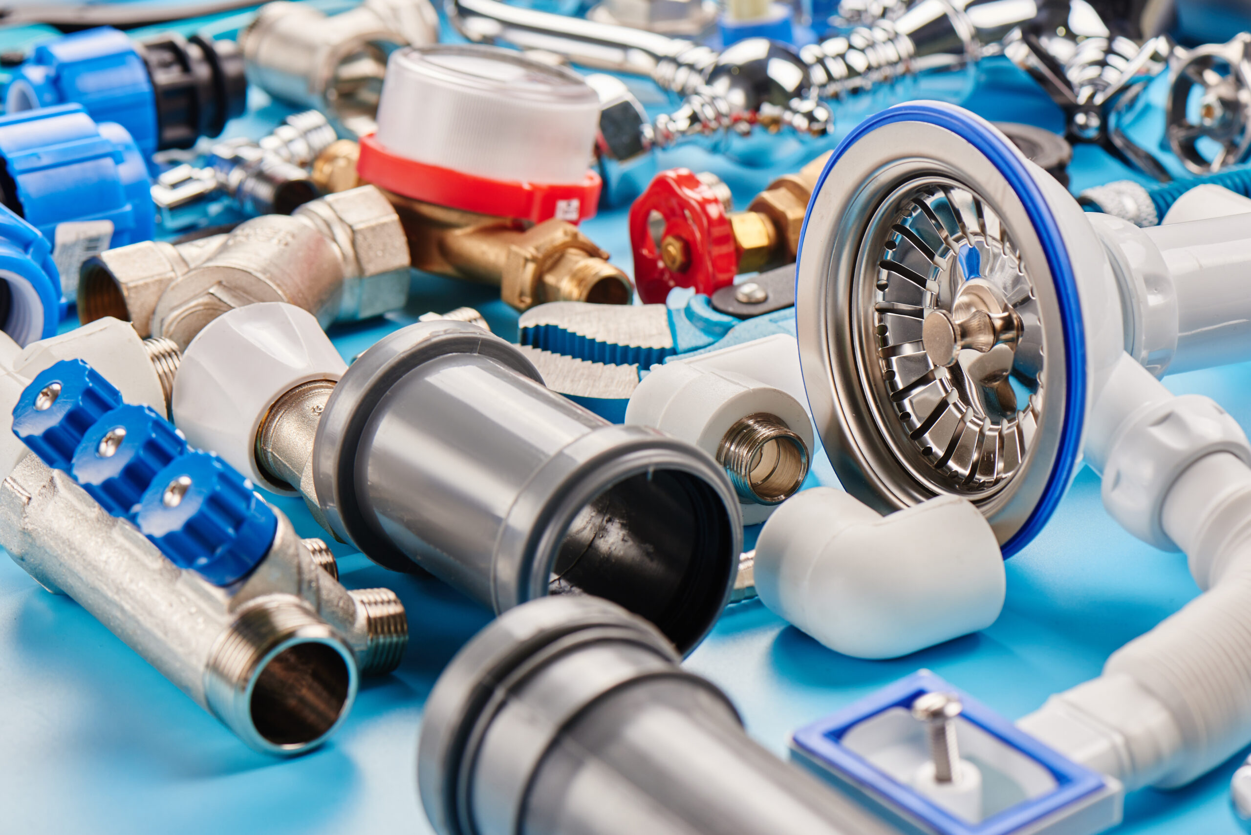 Assorted plumbing parts and fittings, including pipes, valves, connectors, and a sink strainer, arranged on a blue surface.