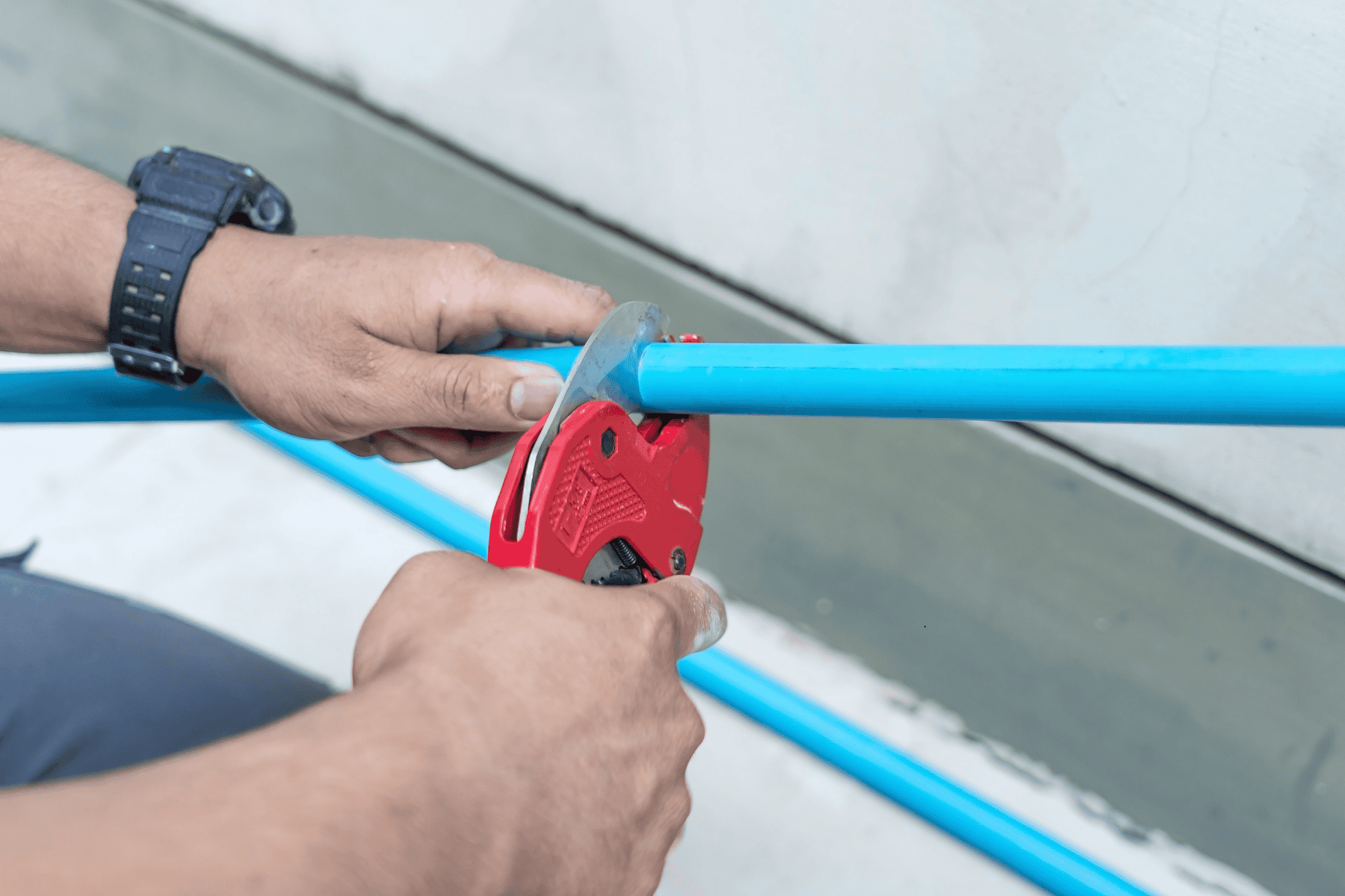 Hands using a red pipe cutter to cut a blue plastic pipe, commonly addressed during homeowner plumbing tips for various plumbing problems.